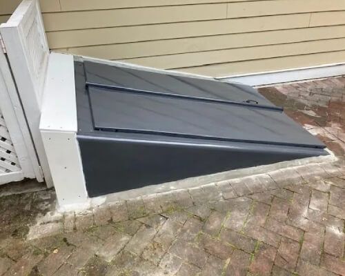 A gray door is sitting on a brick sidewalk next to a house.