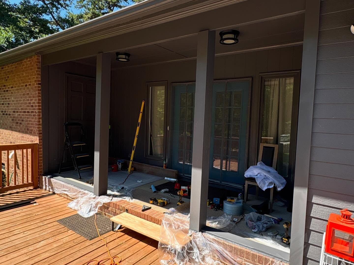 Covered porch under renovation with tools, debris, and plastic sheeting on the floor.