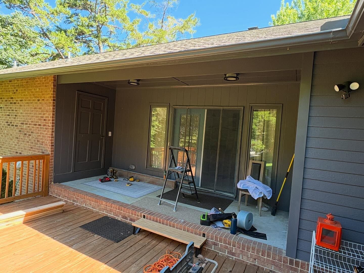 Covered backyard patio with a small porch, brick steps, sliding glass doors, and tools on the floor