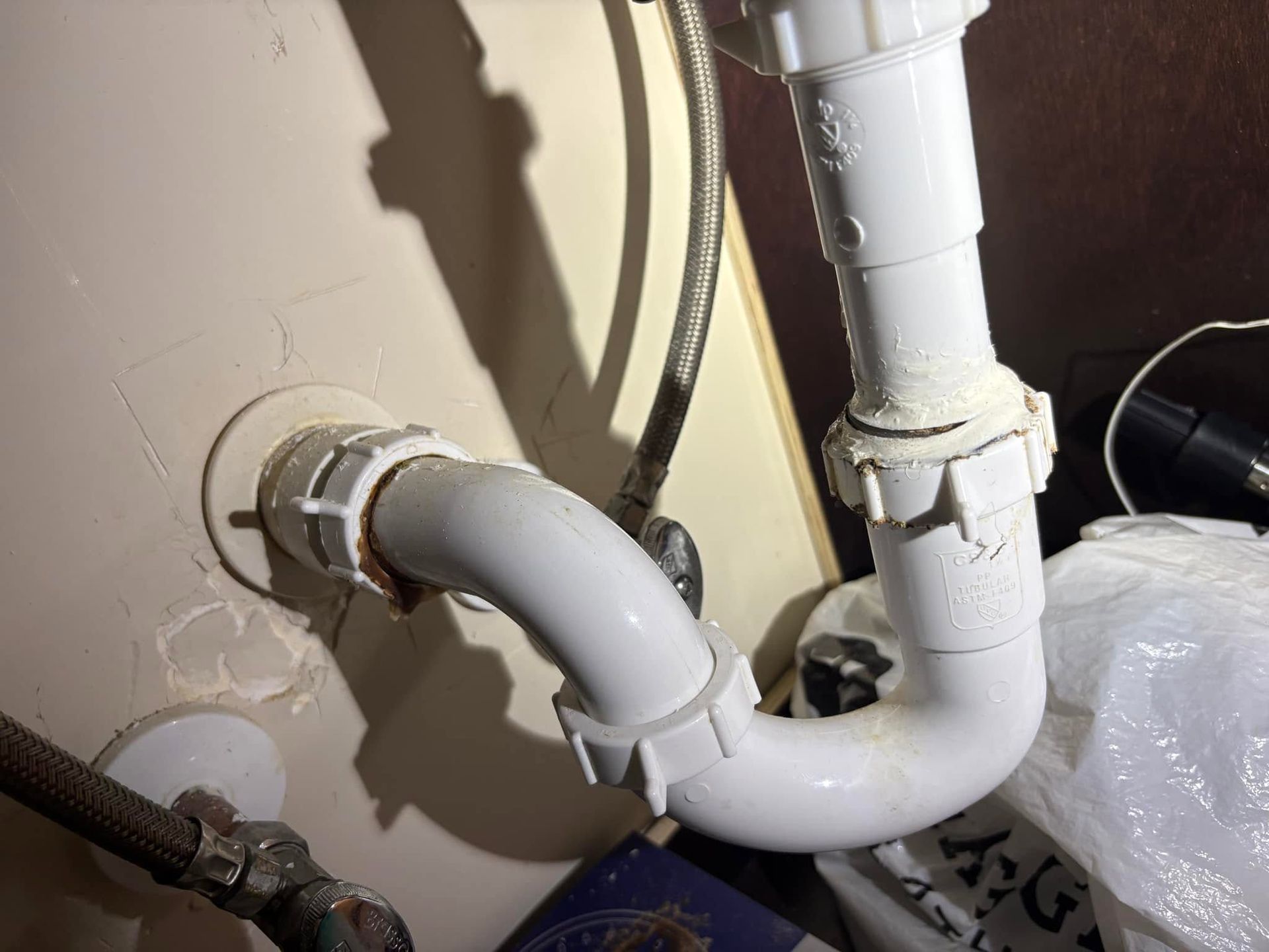 White PVC drain pipes connected to a beige wall under a sink or appliance.