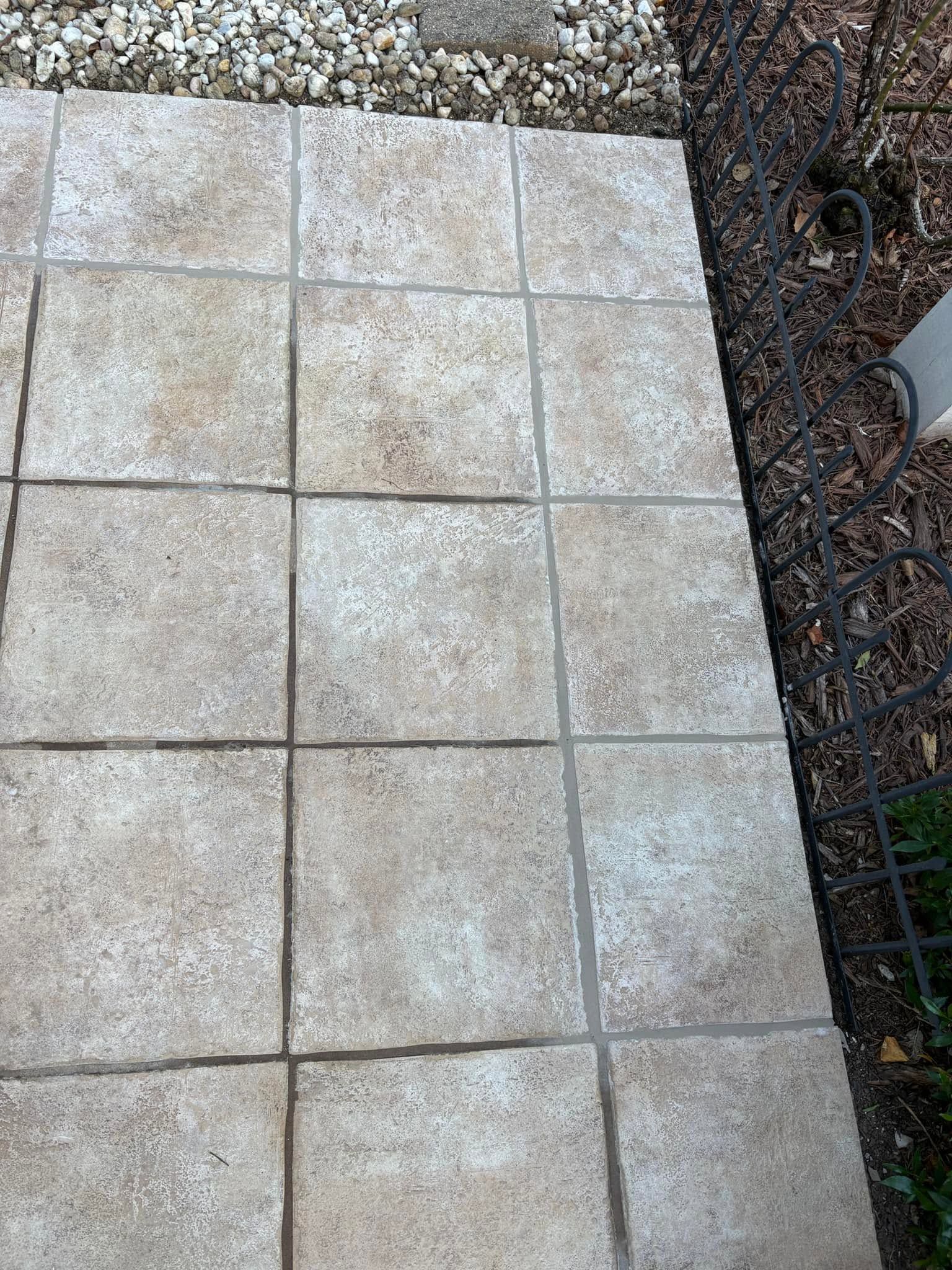 Stone patio tiles beside gravel and a garden bed with a metal fence.