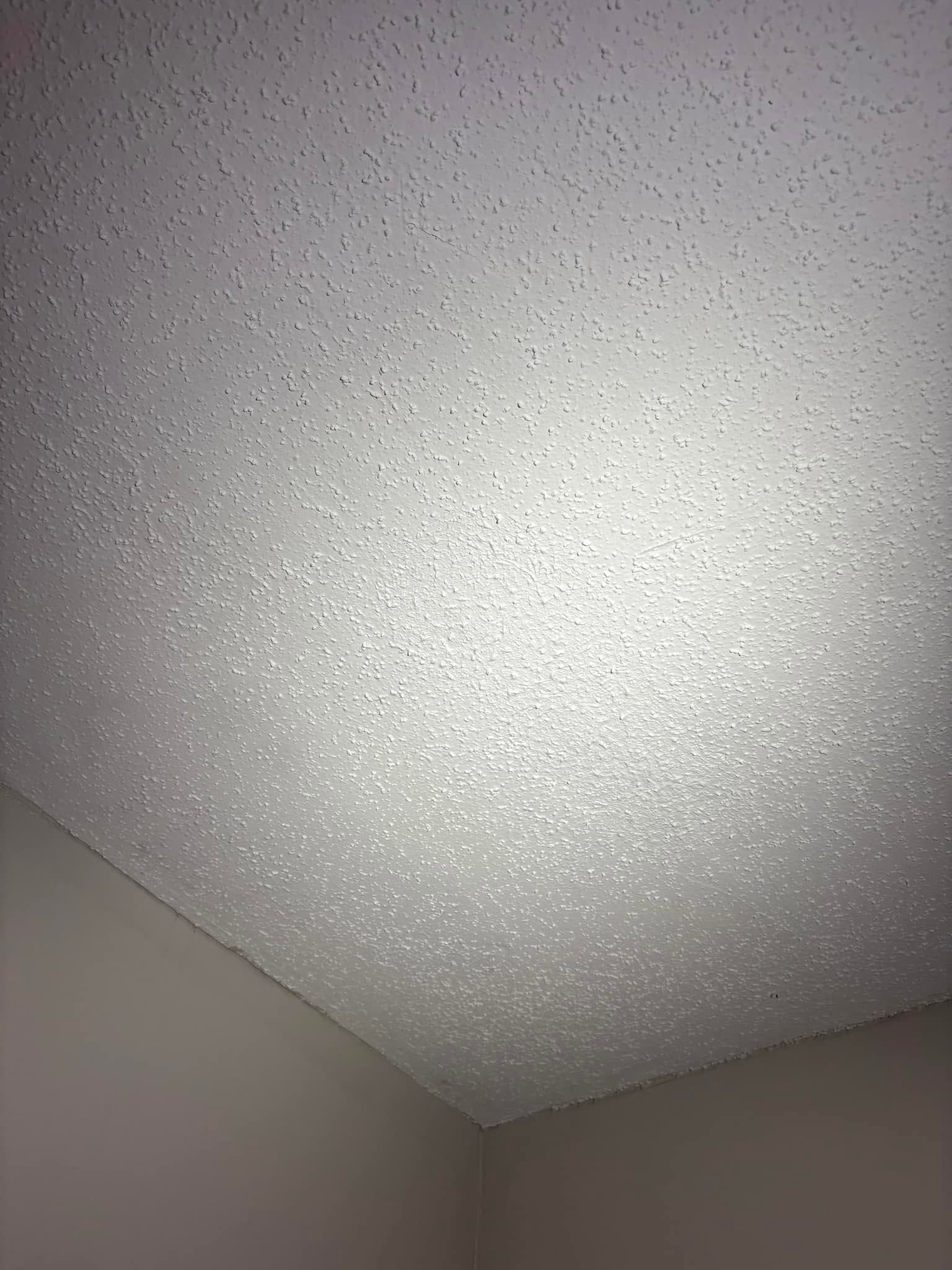 Textured white ceiling corner with gray walls and bright light reflection