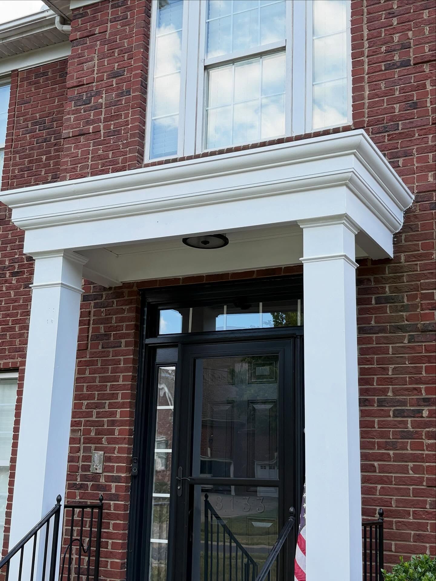 Brick townhouse entrance with white columns and a black door under a small porch