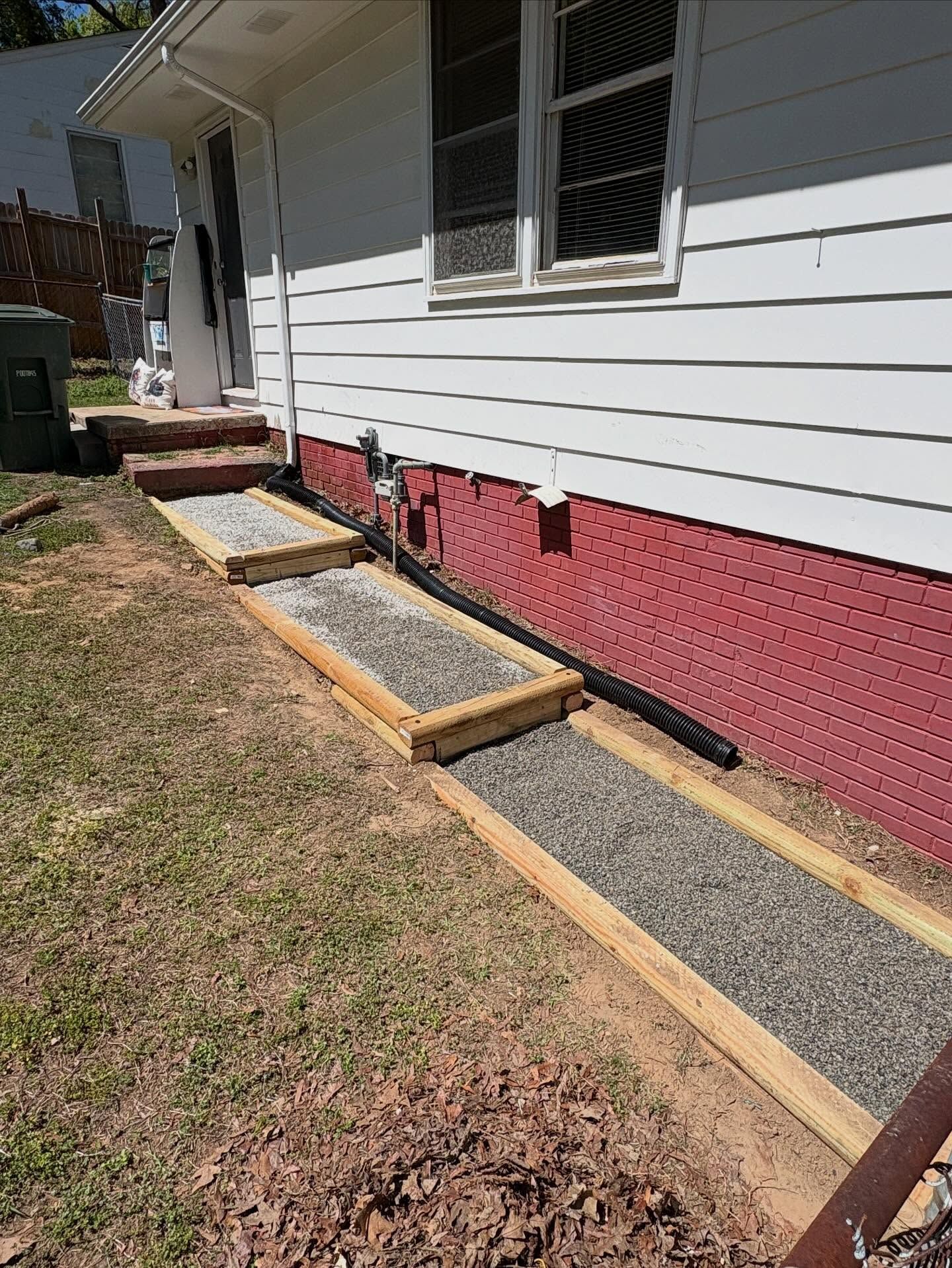 House side with newly built wooden-framed gravel path and raised beds along the foundation