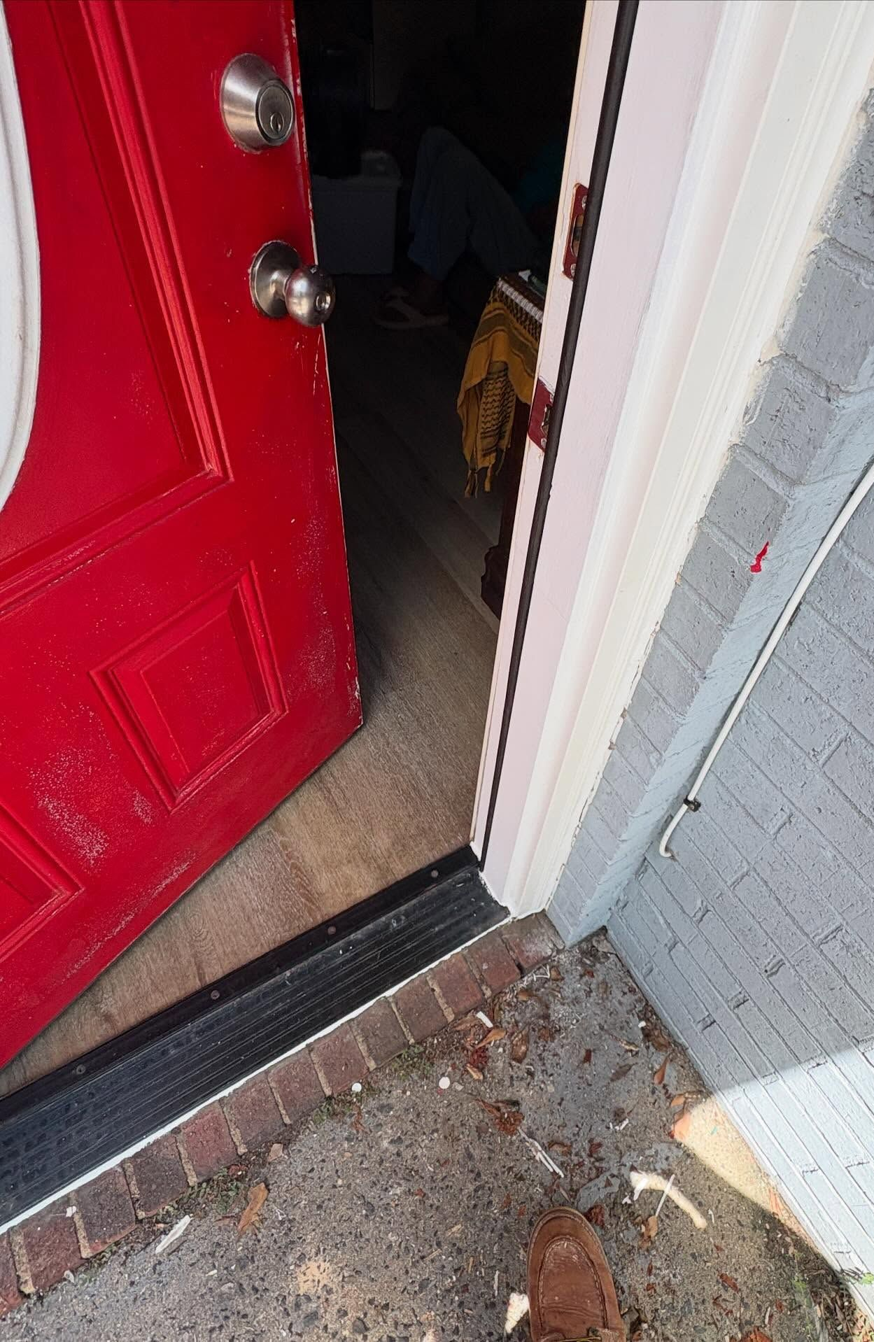 Open red front door with a small dog peeking out from inside onto a stone doorstep.