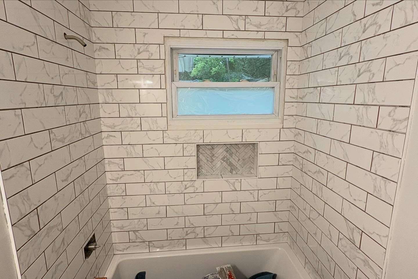 Small tiled room with a window, wall niche, and bare floor under construction