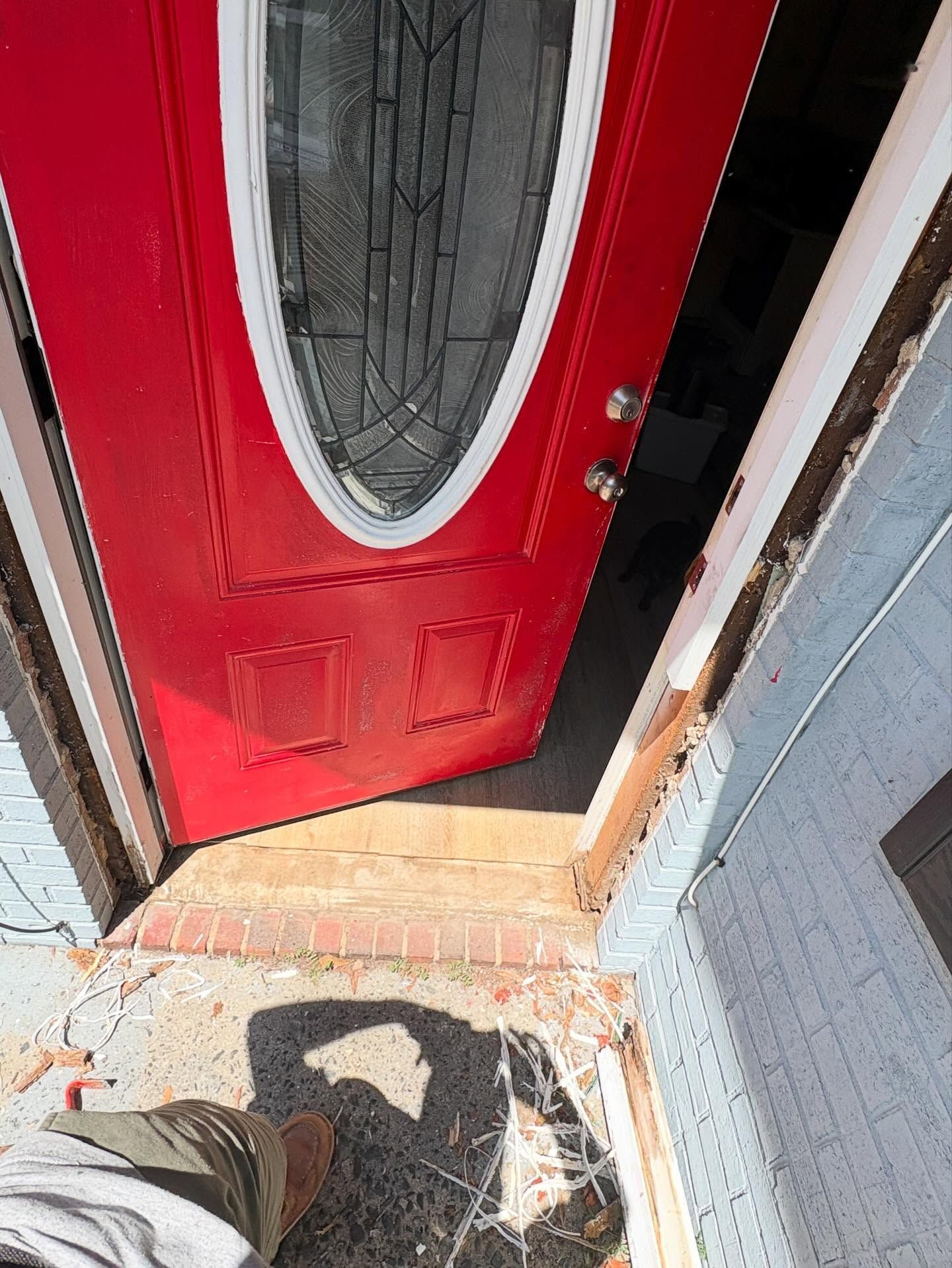 Partially open red front door with oval window, viewed from outside onto a brick doorstep.