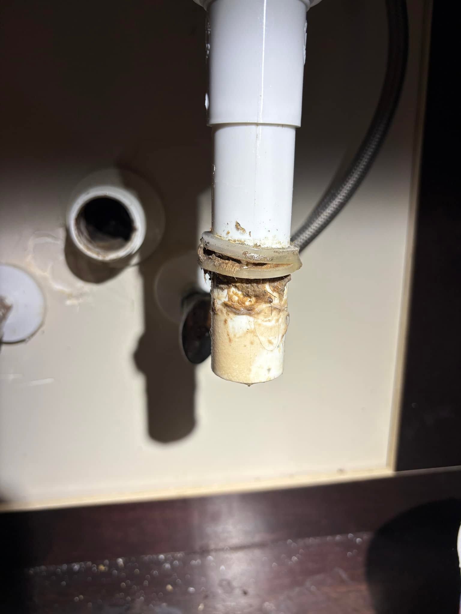 Corroded white drain pipe under a sink with rust buildup and a loose fitting