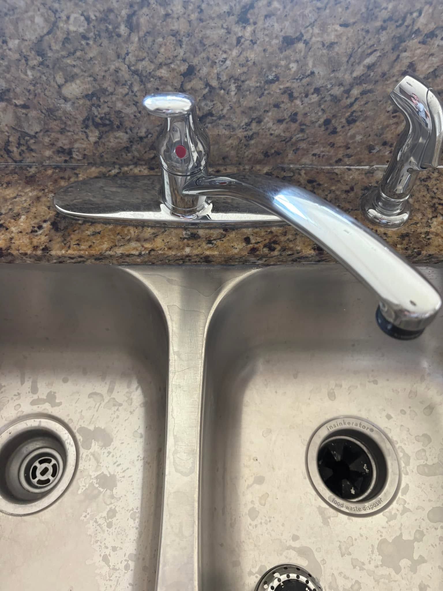 Kitchen sink with a chrome faucet and dirty twin basins against a speckled backsplash
