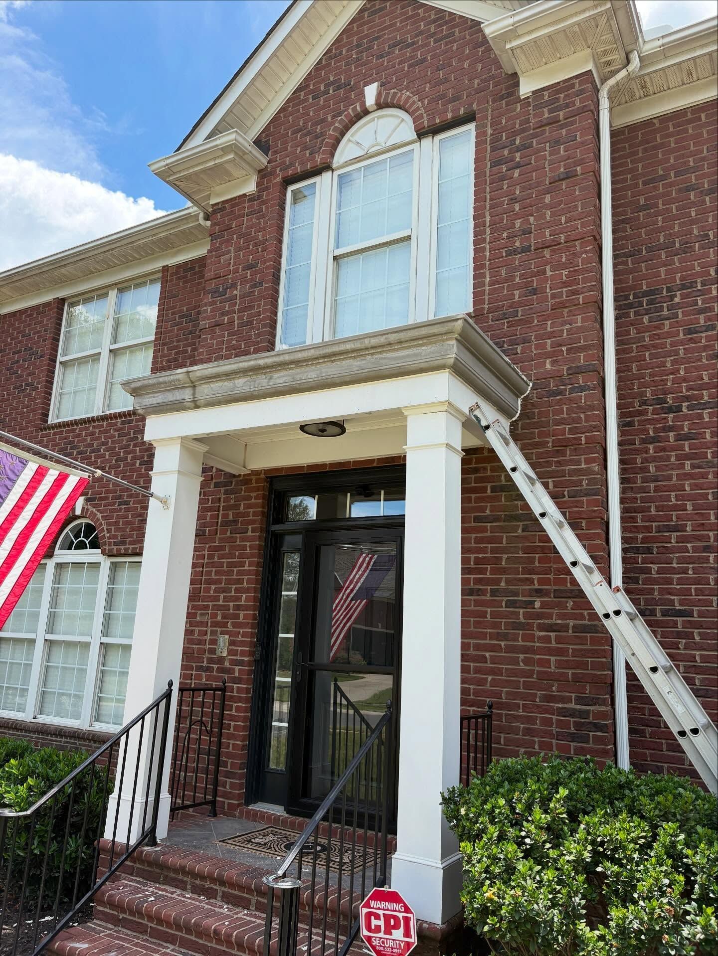 Brick townhouse entrance with black door, white columns, ladder on right, and American flag on the left.