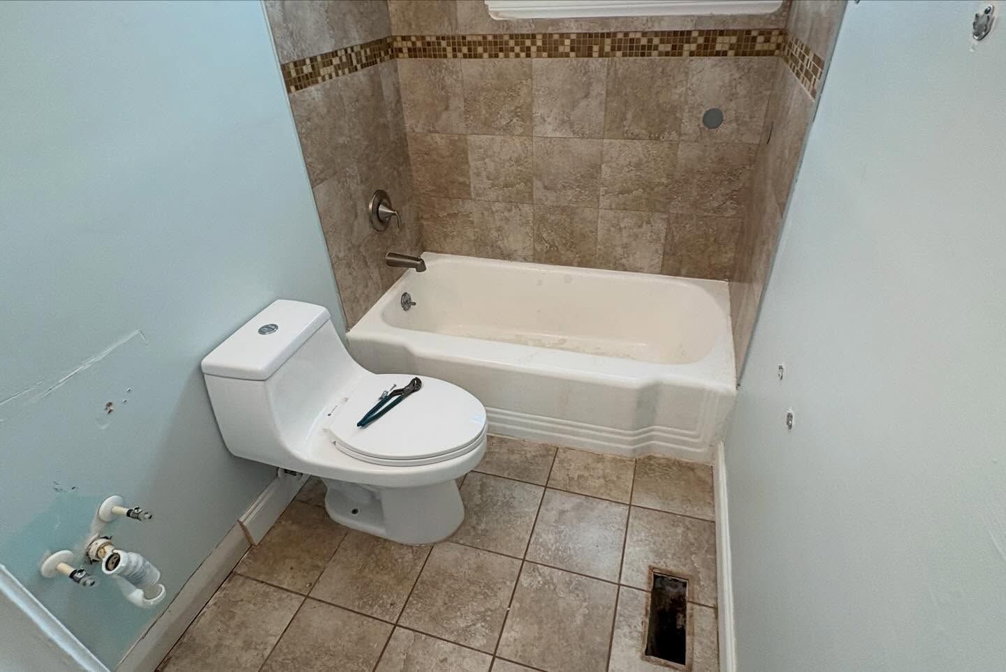 Small bathroom with toilet, bathtub, beige tile walls, and tiled floor.