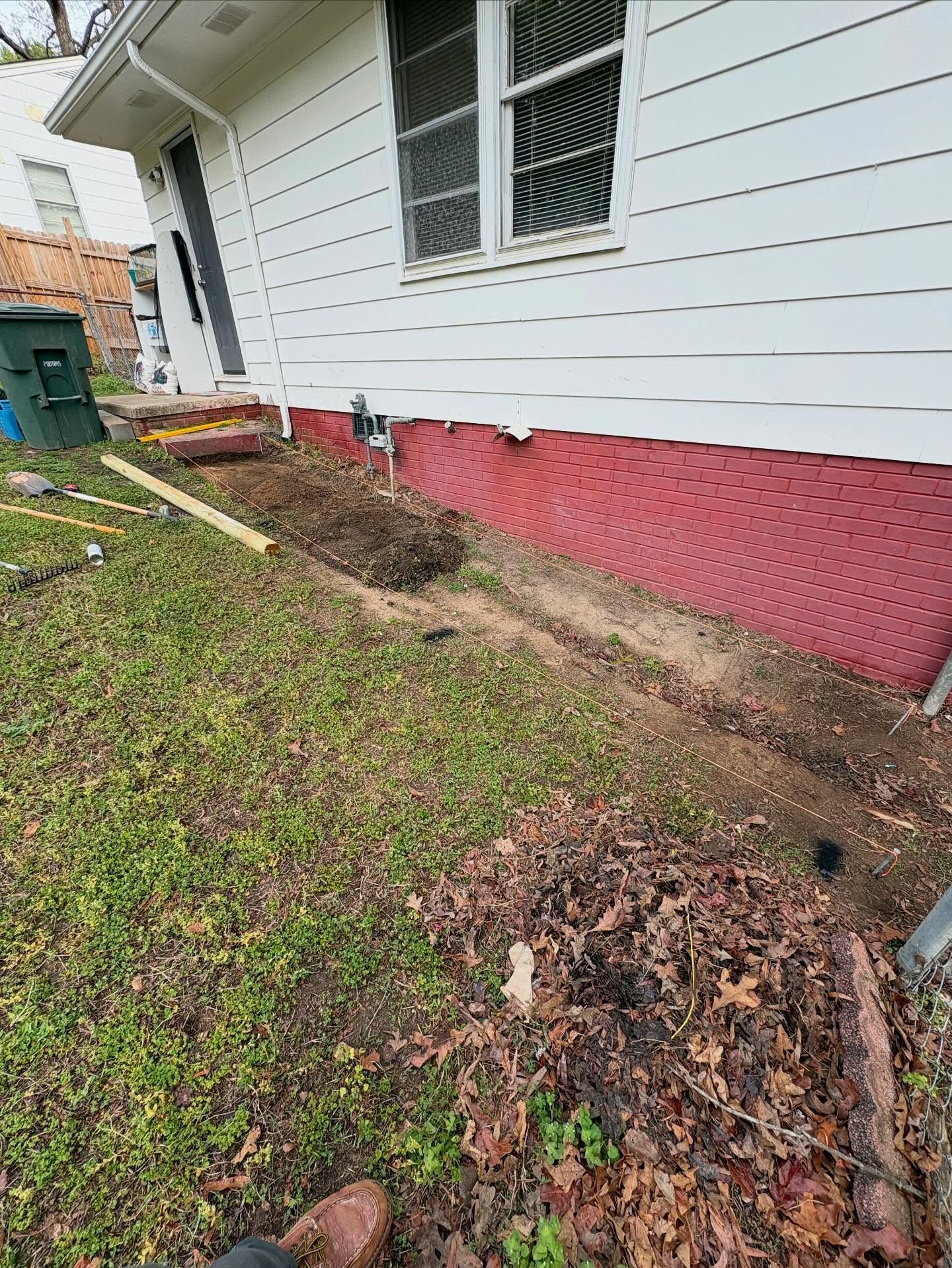 House siding with red foundation skirt and a muddy, eroded strip along the base outdoors