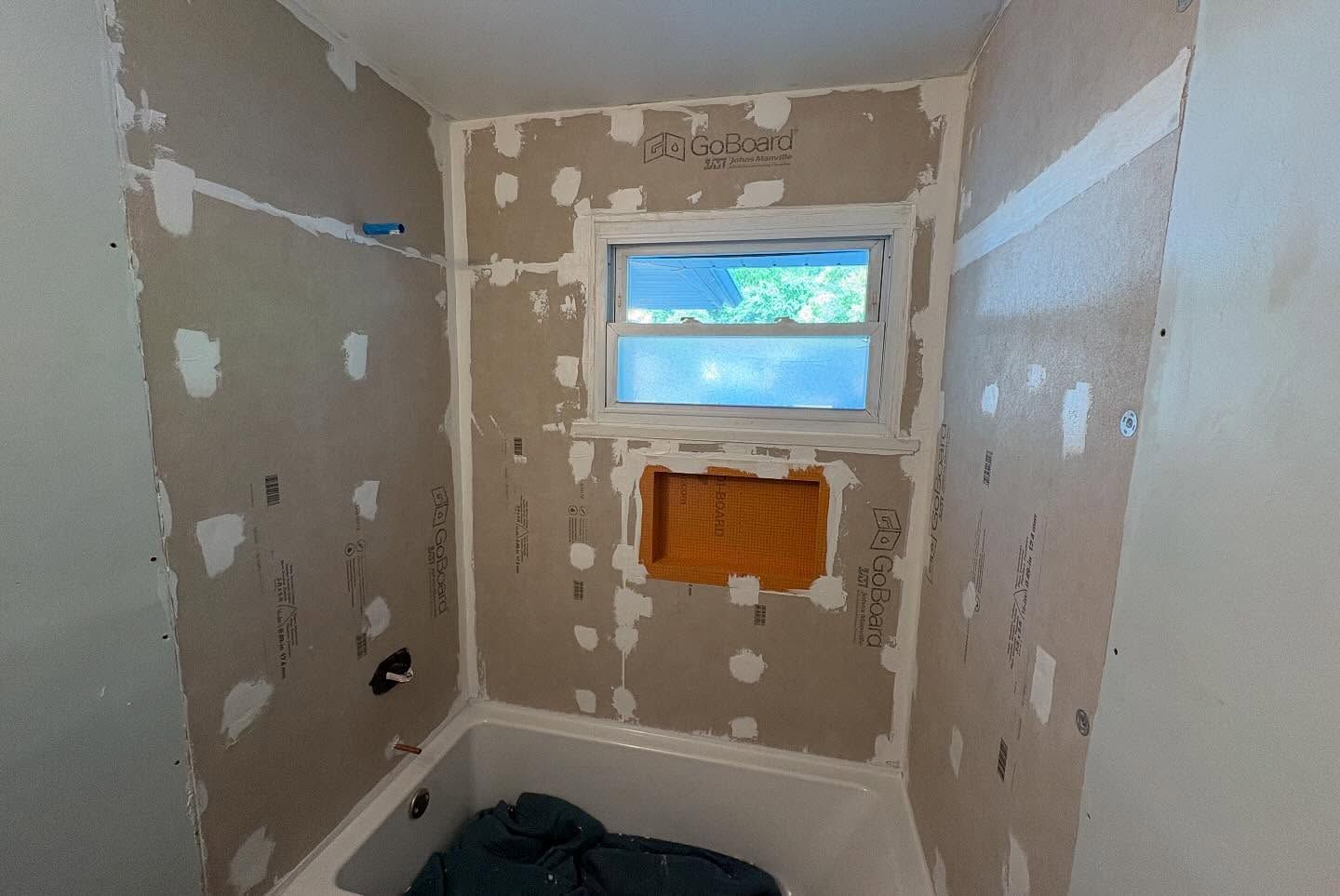 Small unfinished bathroom with patchy drywall, a small window, and exposed plumbing wall opening.
