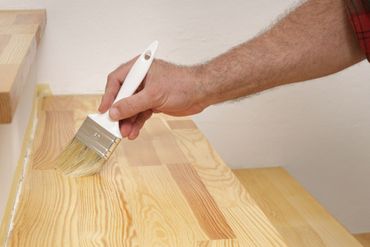 Hand brushing clear finish onto wooden stairs with a white paintbrush