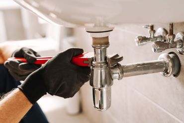 Gloved hands fixing a bathroom sink drain pipe under a white sink
