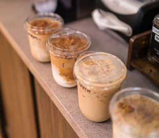 Three iced coffee drinks in clear cups lined up on a counter