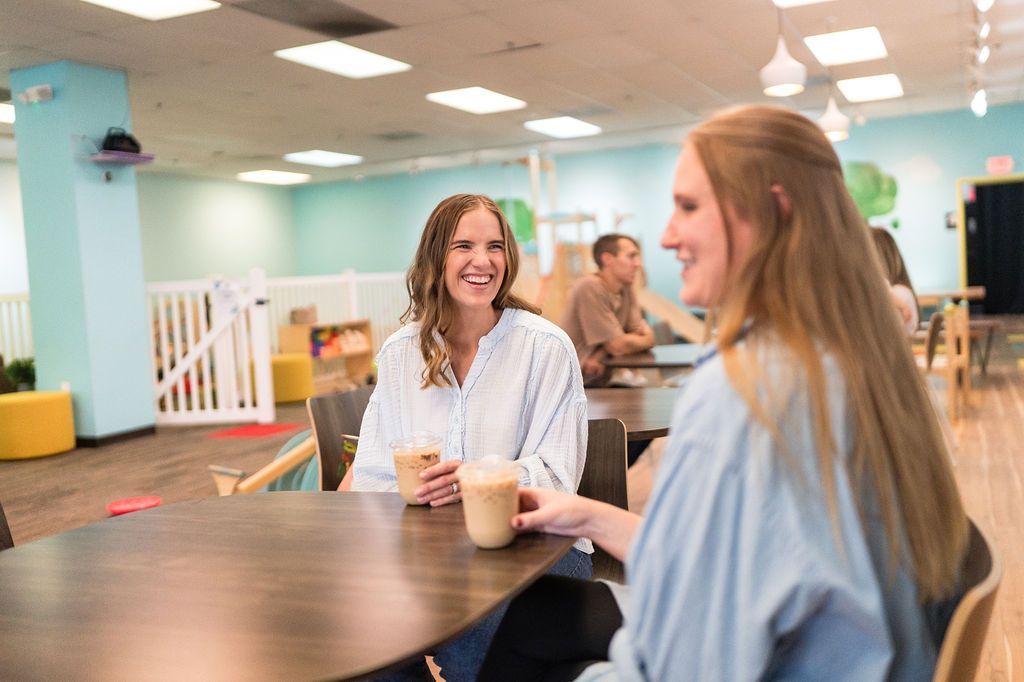 Two people smiling and talking at a table in a bright café-like room
