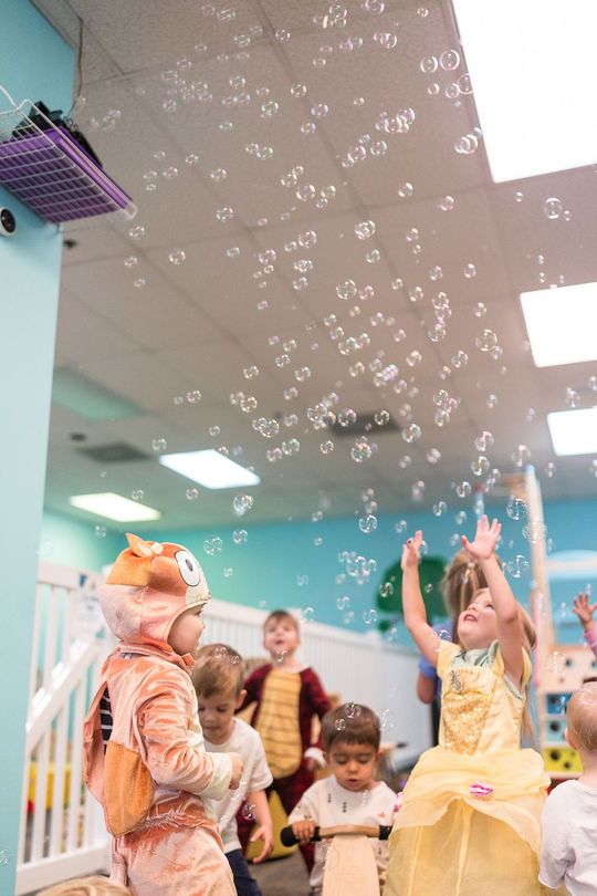 Children reaching for bubbles in a colorful classroom with turquoise walls and ceiling lights