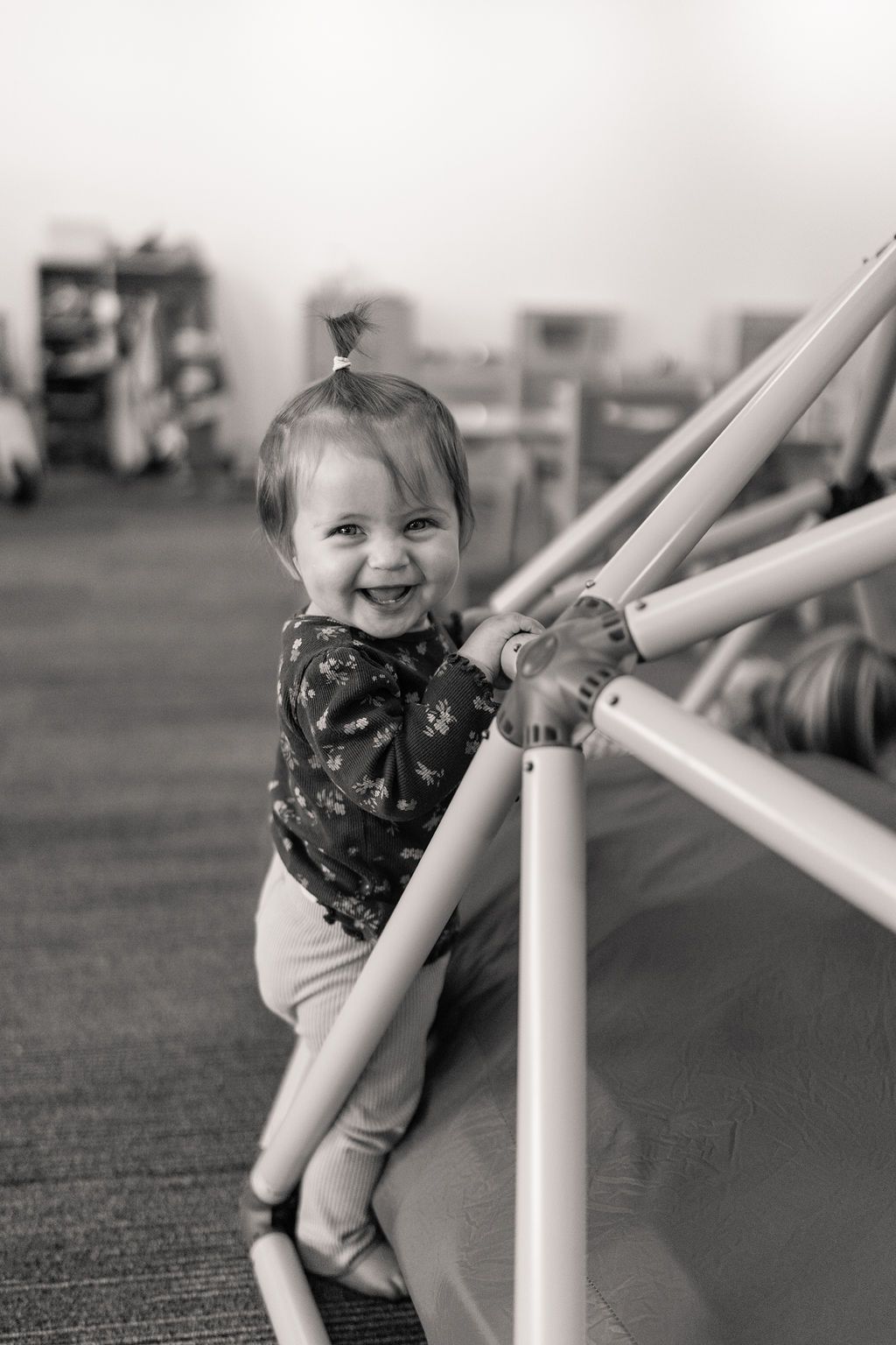 Smiling child holding a white padded climbing frame in a play area