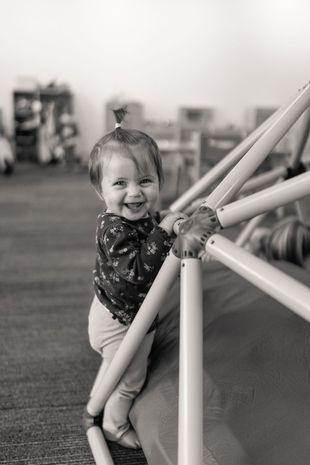 Smiling child standing by a padded play structure in a gym-like indoor space