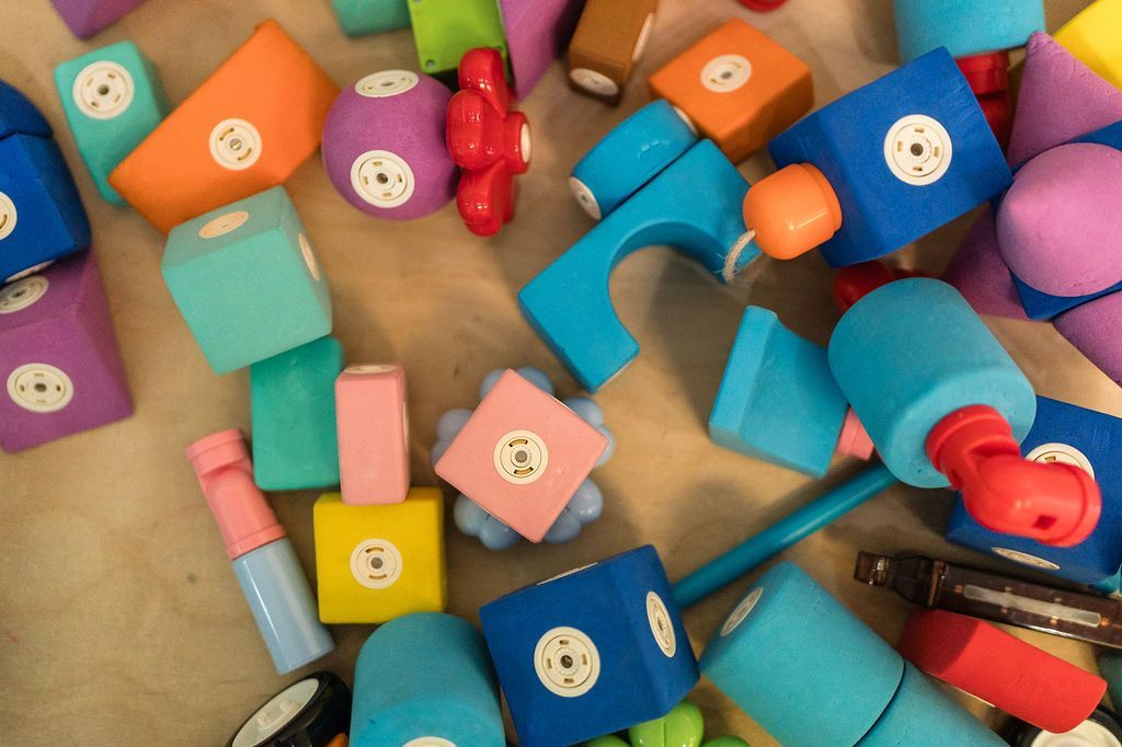 Colorful foam dumbbells scattered on a floor, including pink, blue, orange, purple, and red weights