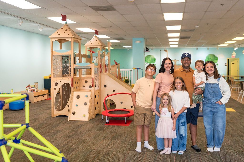 Children standing in a colorful indoor playroom with wooden climbing structures and toys