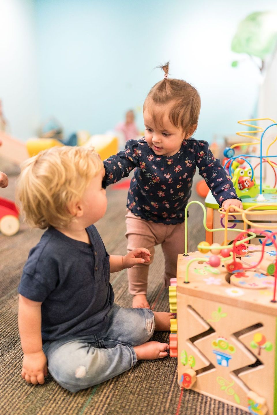 Two toddlers playing with a colorful activity toy in a bright playroom