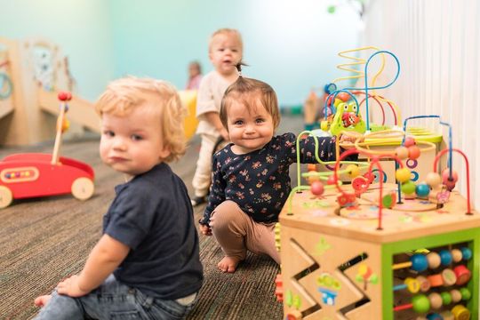 Three toddlers playing with colorful toys in a bright daycare room