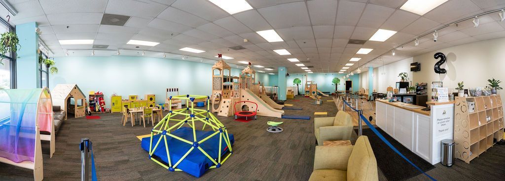 Bright children’s playroom with colorful toys, climbing structures, and couches under a white ceiling