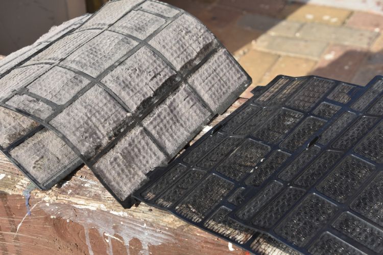 A close up of a dirty air filter on a brick wall.