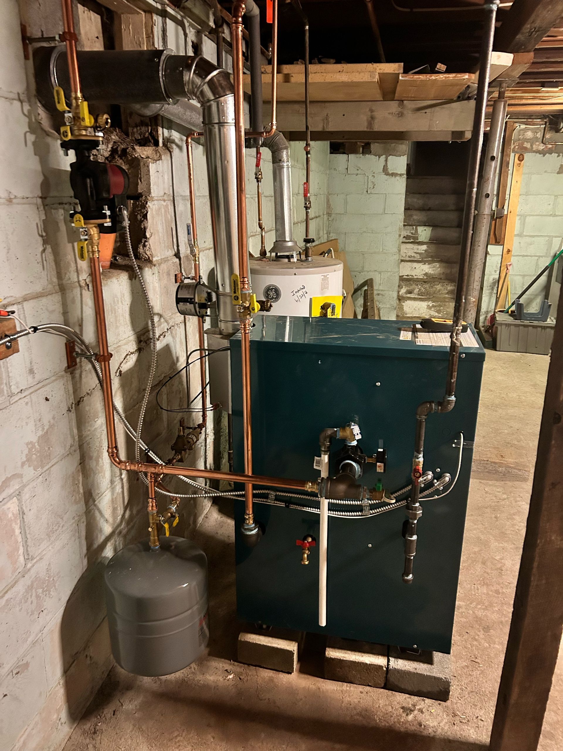 A boiler is sitting in a basement next to a water heater.