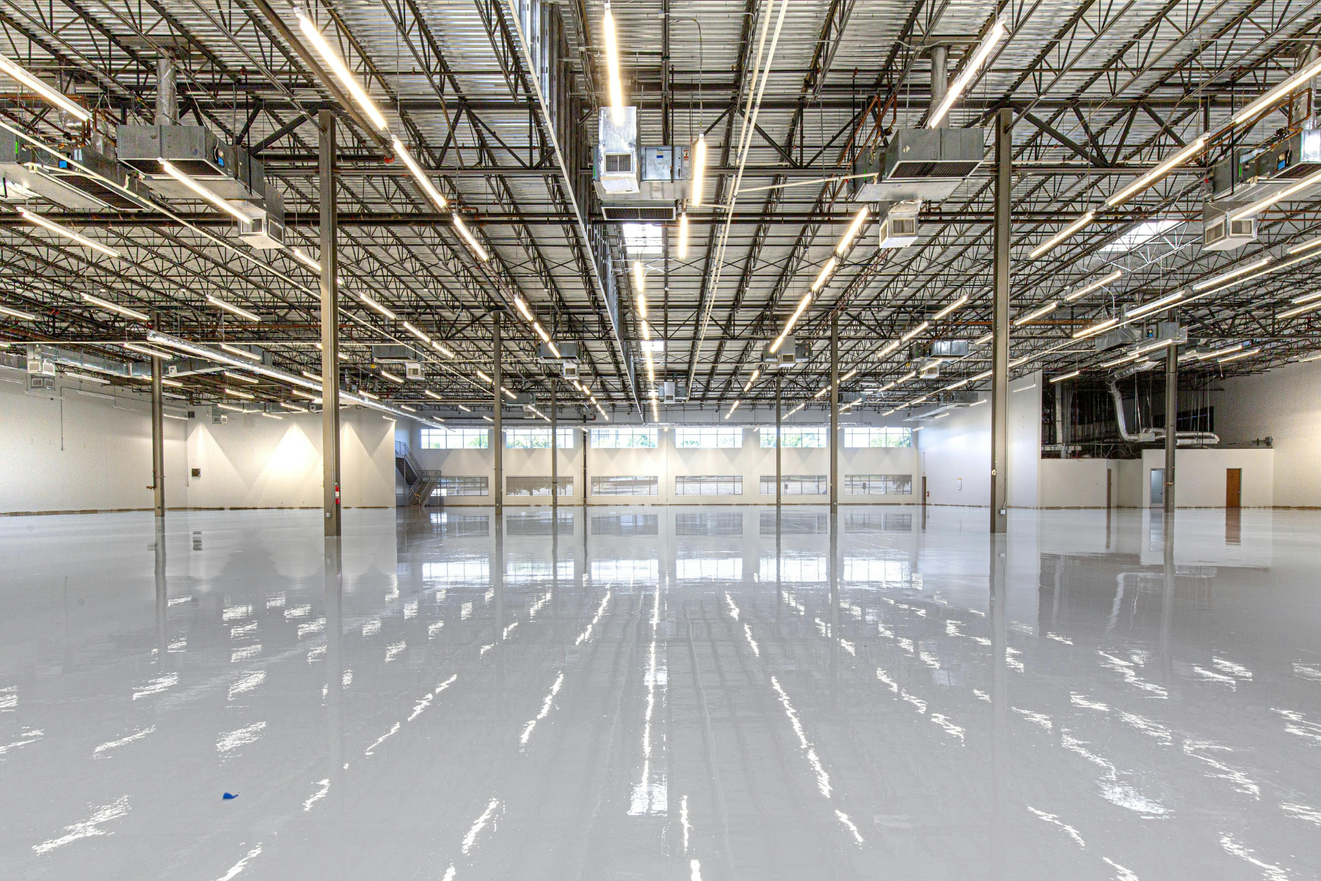 Empty polished warehouse interior with glossy white floor and exposed ceiling beams