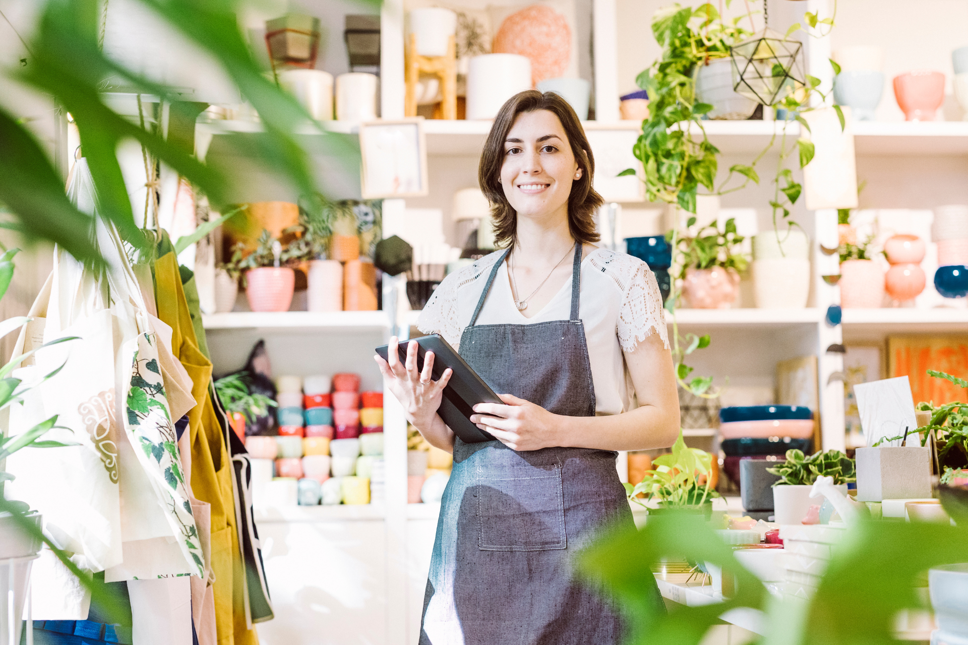 Shop owner smiling in a plant-filled store, holding a notebook and wearing an apron
