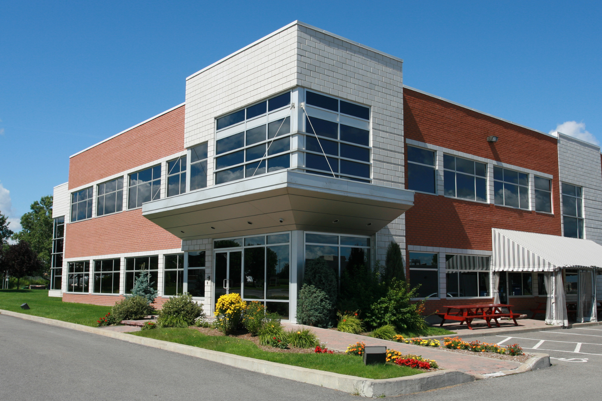 Modern two-story brick-and-glass building with landscaped entrance under a blue sky