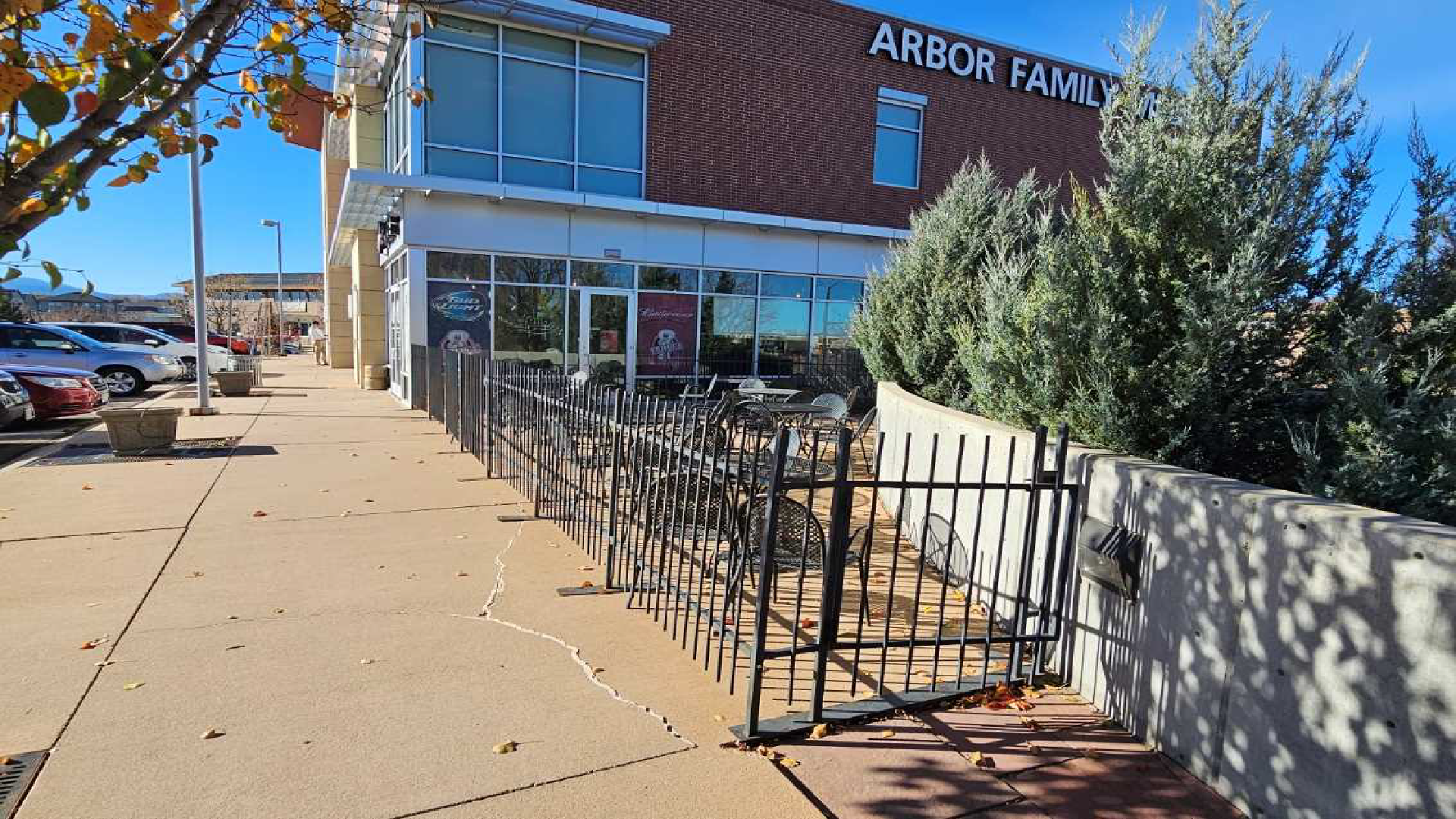 Storefront with a metal fence and sidewalk, with “Arbor Farm” sign above the entrance on a sunny day