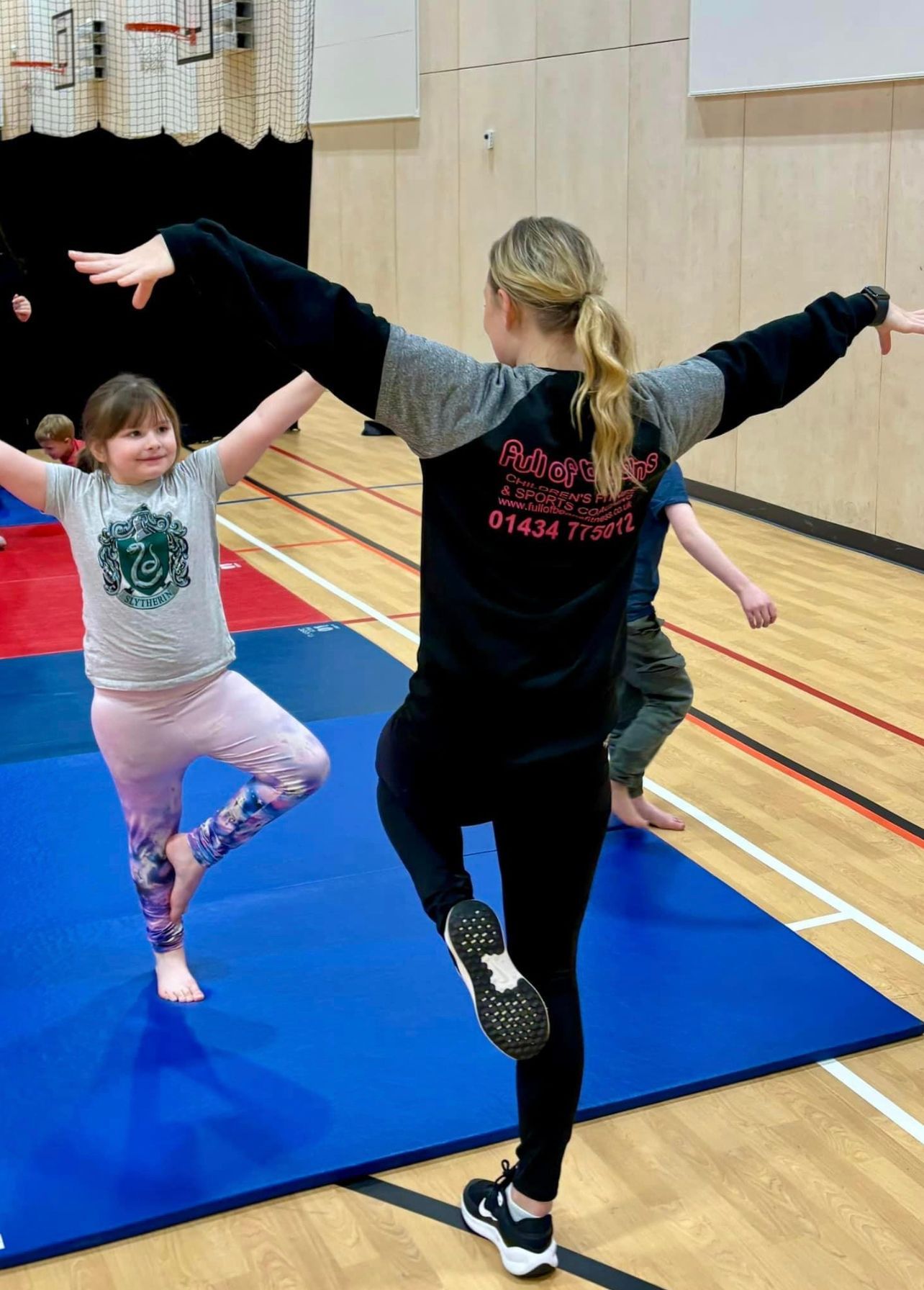 A woman is teaching a young girl how to do a yoga pose in a gym.