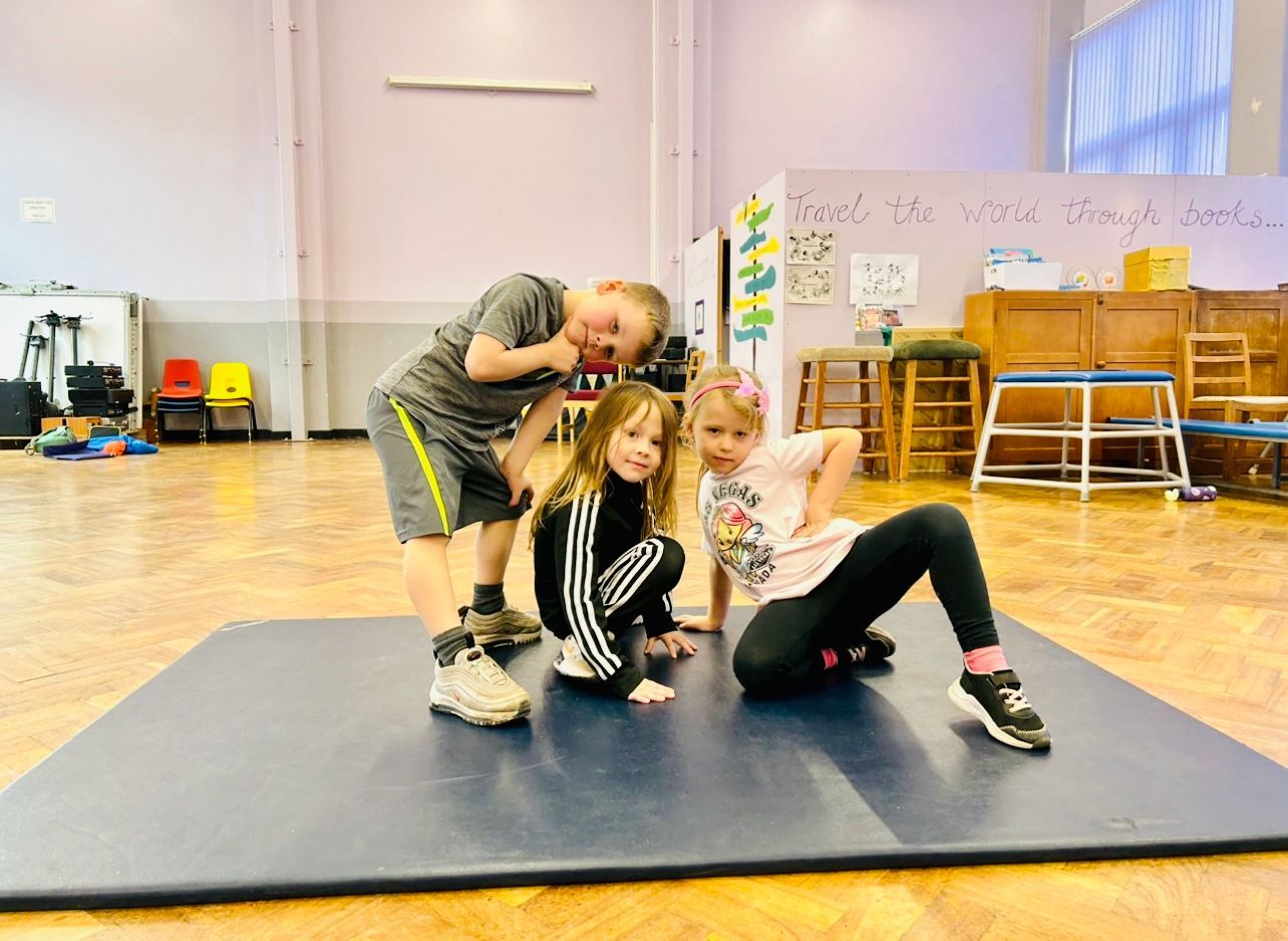 Three children are posing for a picture on a mat in a gym.