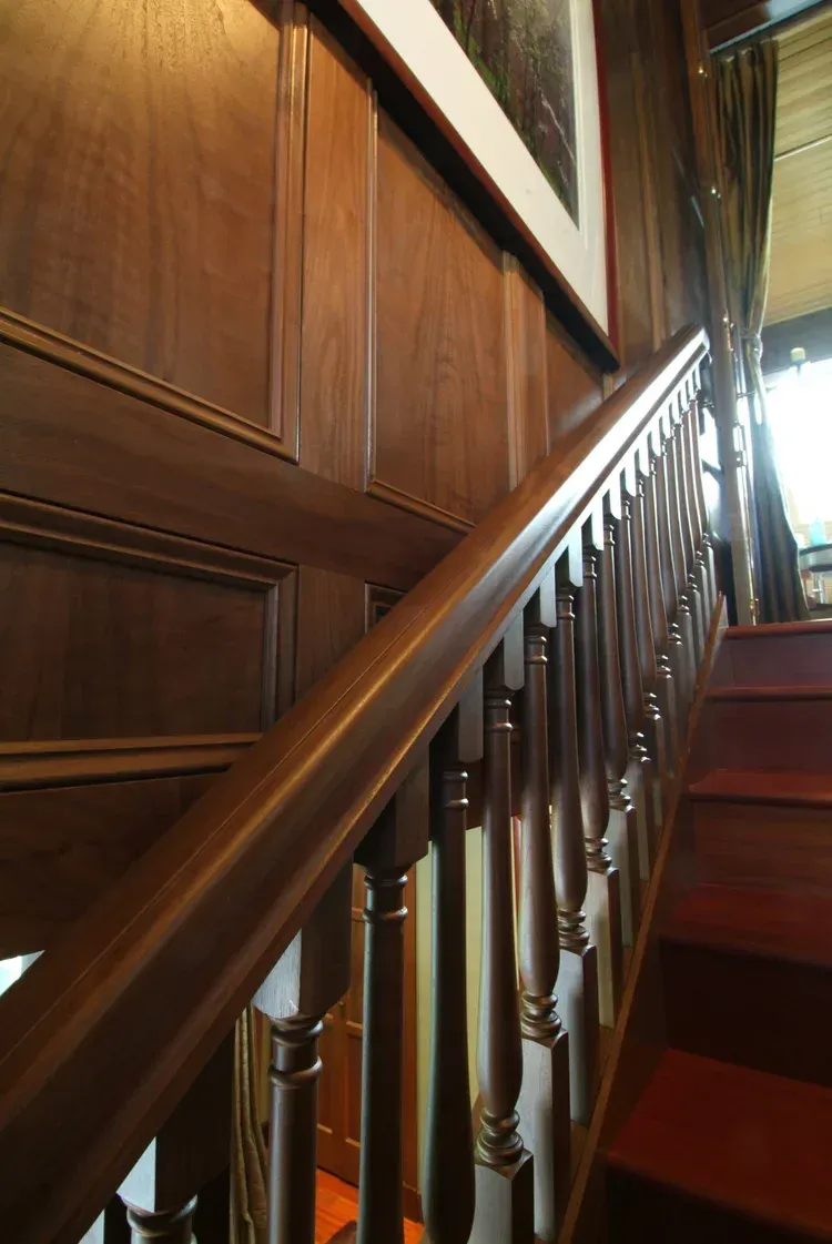 Wooden staircase with polished banister and panelled wall in a dim interior