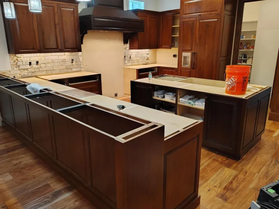 Kitchen with dark wood cabinets and granite island countertops under renovation, with an orange bucket on the counter