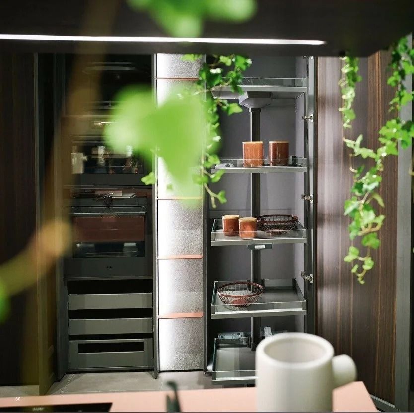 Modern kitchen with open shelving, dark cabinets, plants, and a white mug in the foreground