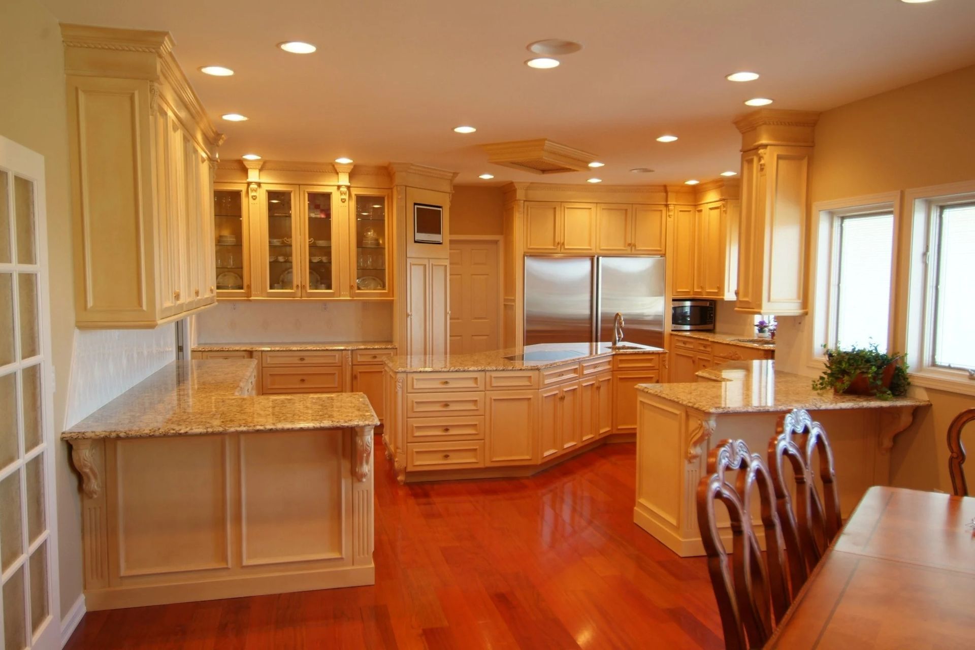 Bright, spacious kitchen with wooden floors, cream cabinets, granite counters, and stainless steel appliances