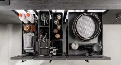 Overhead view of a black kitchen drawer organizer with utensils, cups, and plates neatly arranged