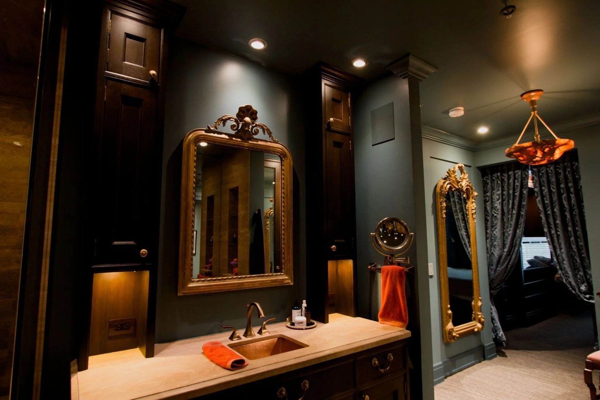Elegant bathroom with gold-framed mirrors, dark walls, marble vanity, and warm lighting