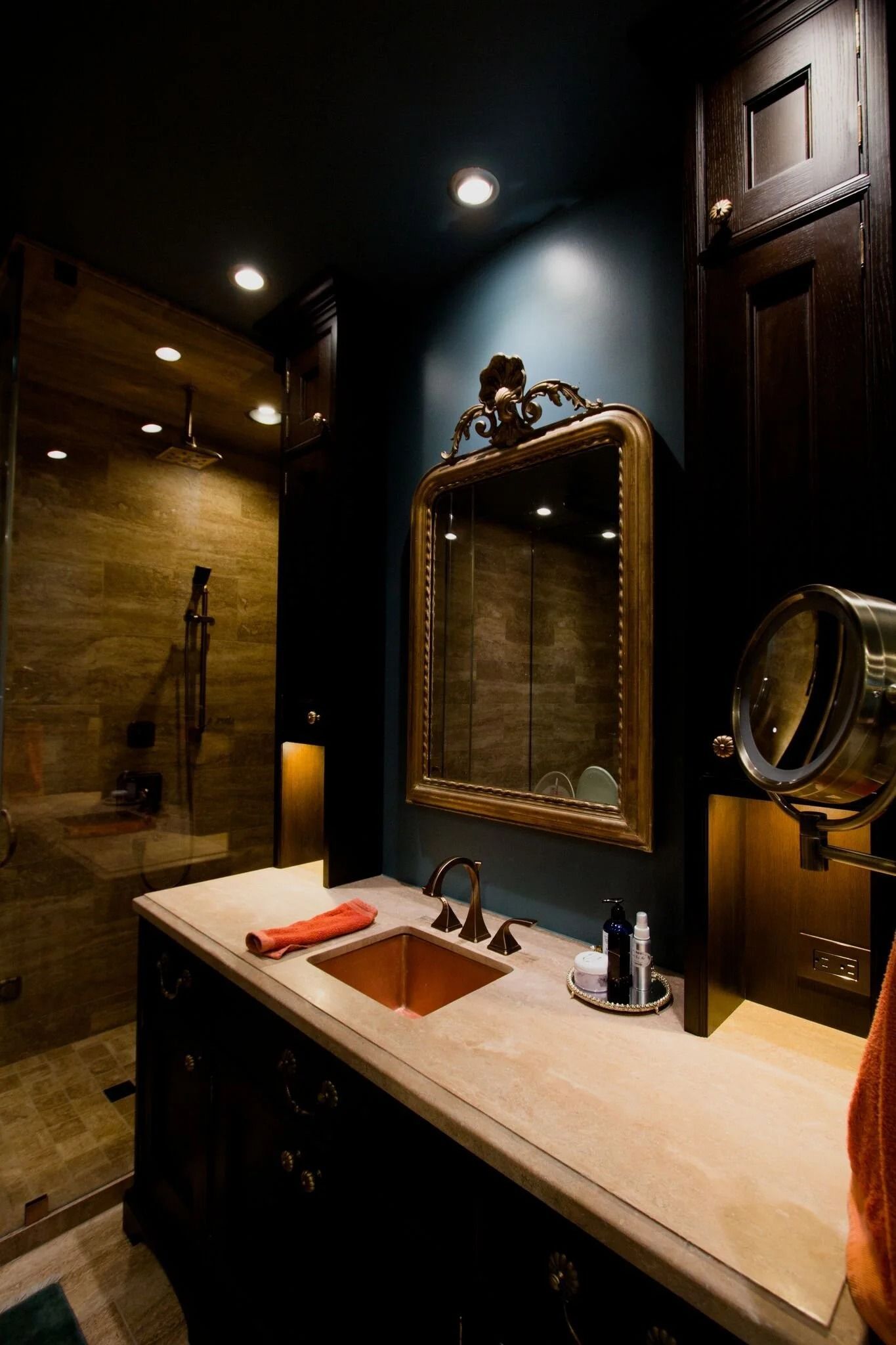 Dimly lit bathroom with copper sink, large mirror, shower, and dark wood walls.