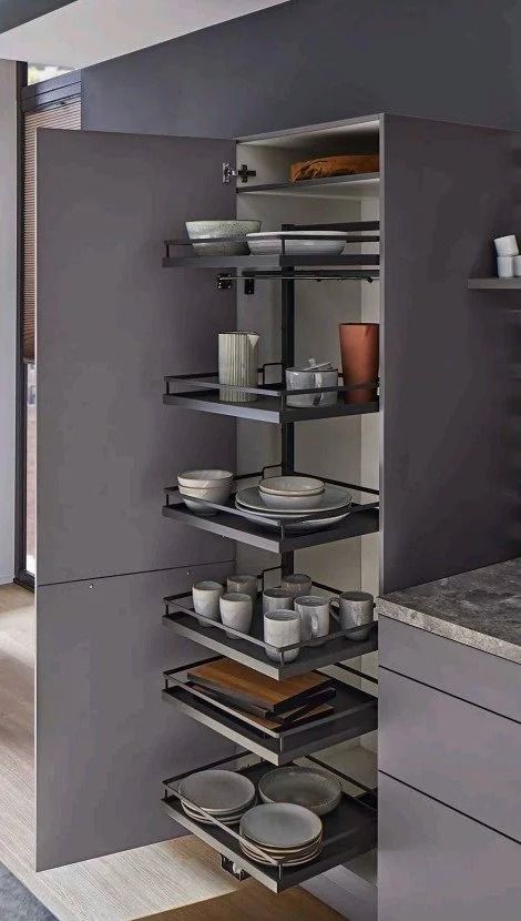 Open kitchen cabinet with pull-out shelves, neatly holding plates, bowls, jars, and cookware.