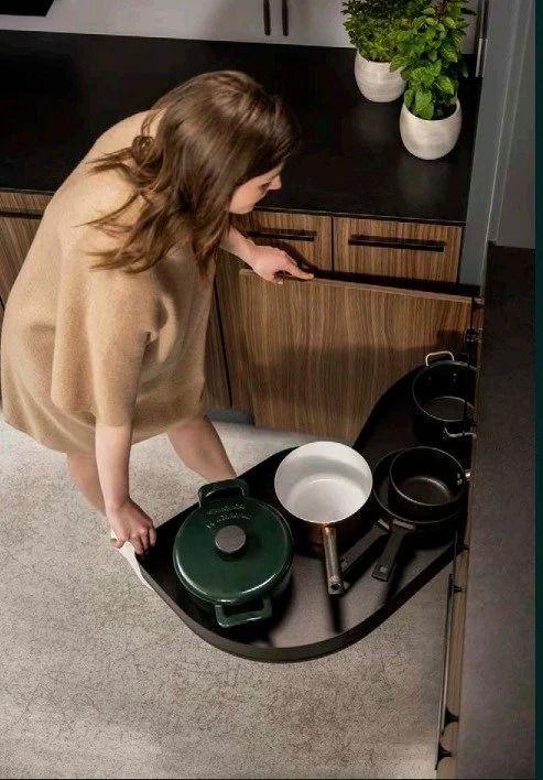 Woman loading green and white cookware into a rotating kitchen cabinet organizer