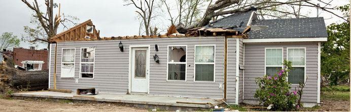 Damaged gray house with roof torn off, showing storm damage in a residential neighborhood