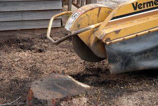 Yellow Vermeer machine bucket digging in dirt beside a curb