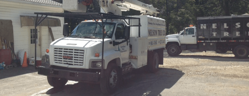 White utility truck parked outside a warehouse in a dusty yard, with another truck in the background.