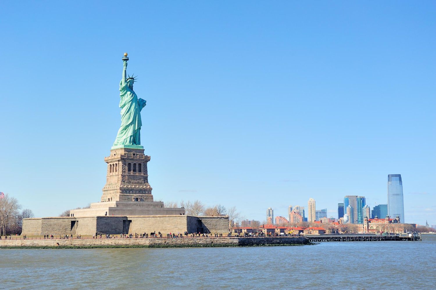 Statue of Liberty on Liberty Island with Manhattan skyline across the water under a clear blue sky